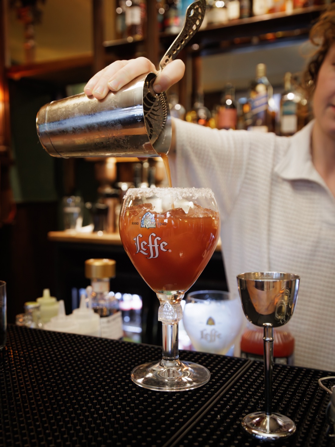A bartender straining a cocktail into a salt-rimmed Leffe glass