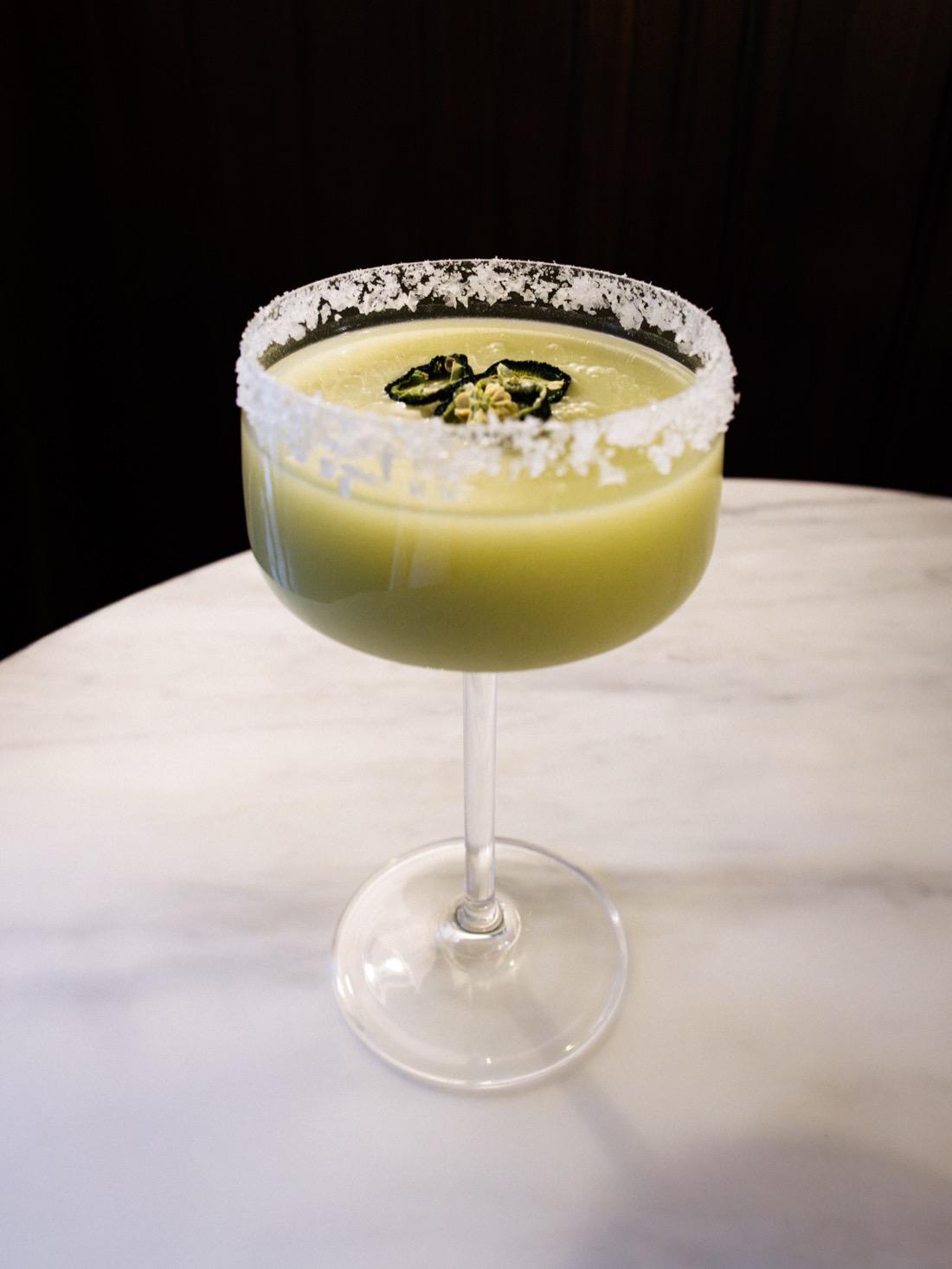 A pale green cocktail in a salt-rimmed coupe, garnished with dried chilli