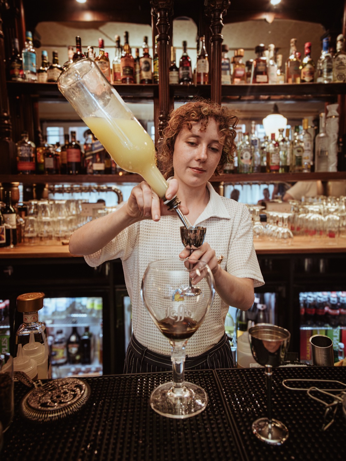 A bartender pouring a measure in front of the back bar